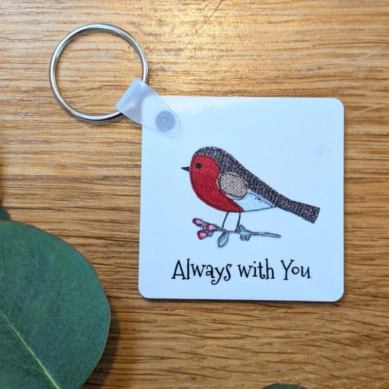 Square robin keyring reading Always with you, on a wooden table with eucalyptus